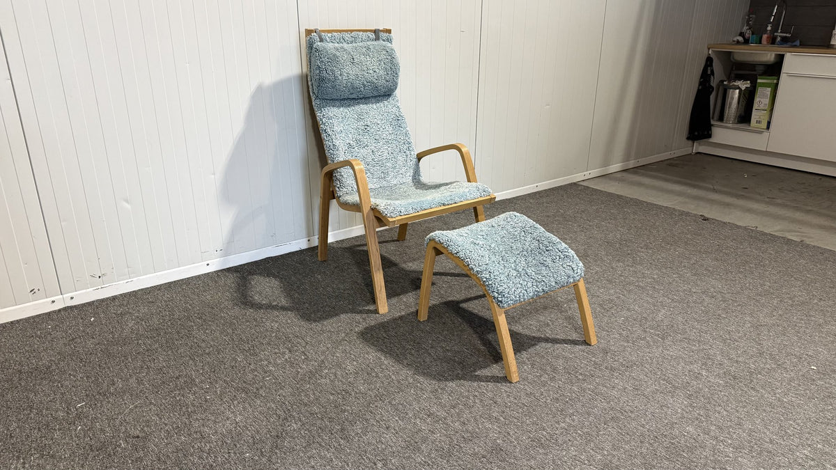 Blå fåtölj i fårull med fotpall sedd snett framifrån